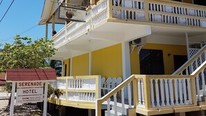 A two-story hotel with a yellow facade, a balcony on the upper floor, and a staircase leading to the entrance. - Serenade Hotel (Placencia)