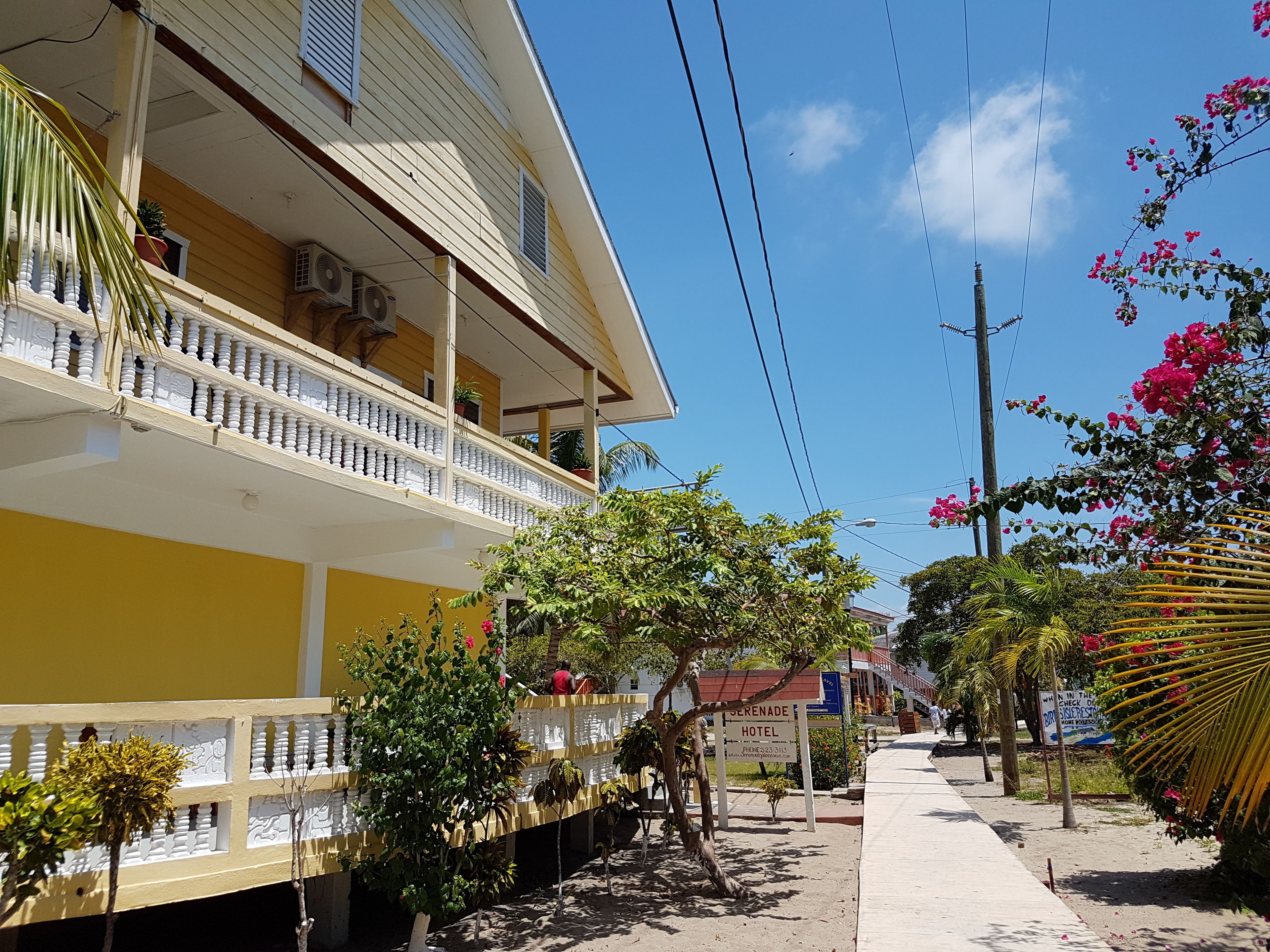 A hotel with a yellow facade, a balcony with white balustrades, and a sign indicating it is a hotel.