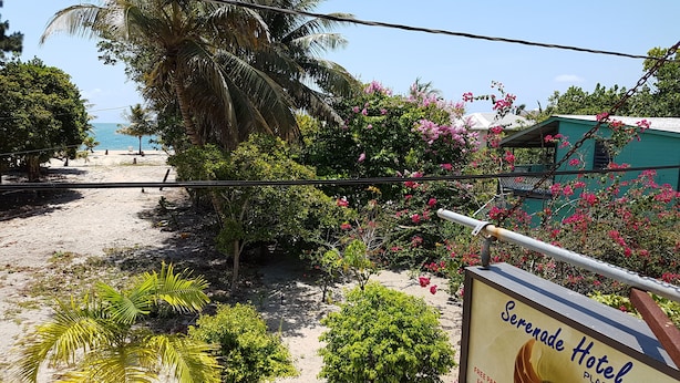 A sign for the Serenade Hotel with a view of the beach and palm trees. - Serenade Hotel (Placencia)