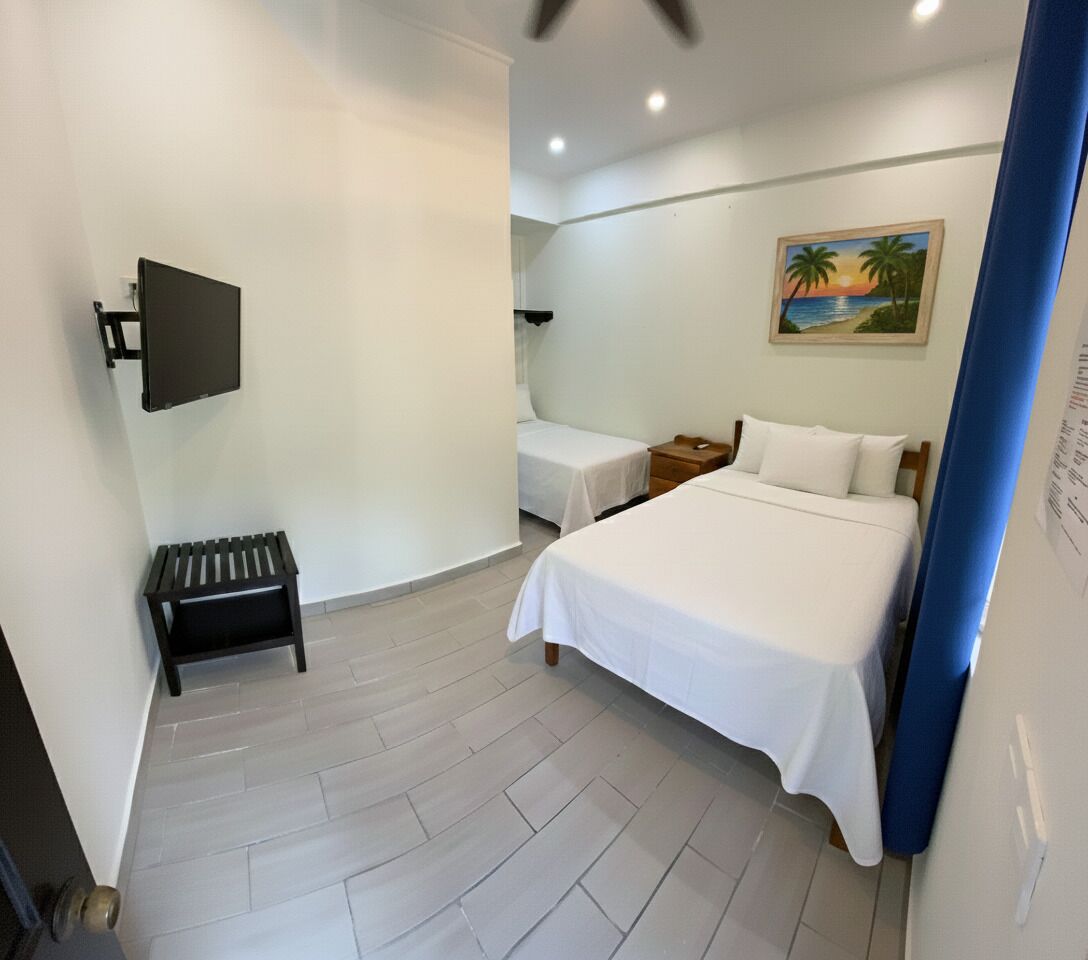 A hotel room with a large bed, a smaller bed, a desk, a chair, a bench, a TV, and a painting on the wall.