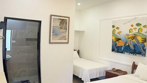 A hotel room with a bed, two bedside tables, a ceiling fan, a painting of sea turtles, and a glass door leading to a bathroom. - Serenade Hotel (Placencia)