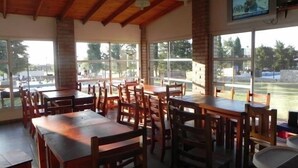 A restaurant with wooden tables and chairs, large windows, and a TV mounted on the wall.