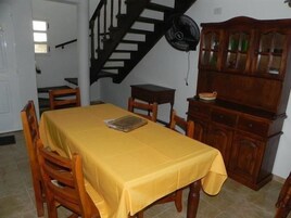 Un comedor con una mesa amarilla, sillas de madera, una escalera y un armario de madera con puertas de cristal.