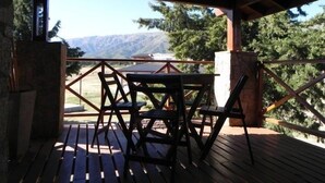 A wooden deck with a table and chairs, overlooking a mountainous landscape.