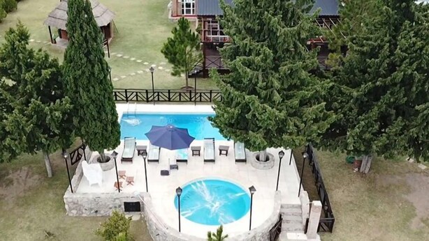An outdoor swimming pool with lounge chairs and umbrellas, surrounded by stone walls and trees.