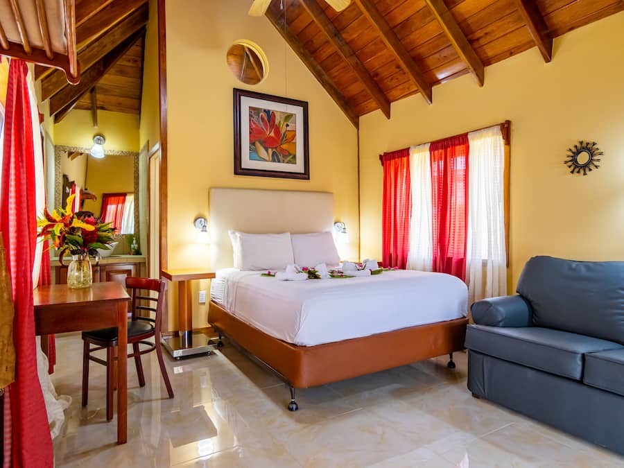 Una habitación de hotel con cama, sofá, mesa de comedor con sillas y un florero con flores.