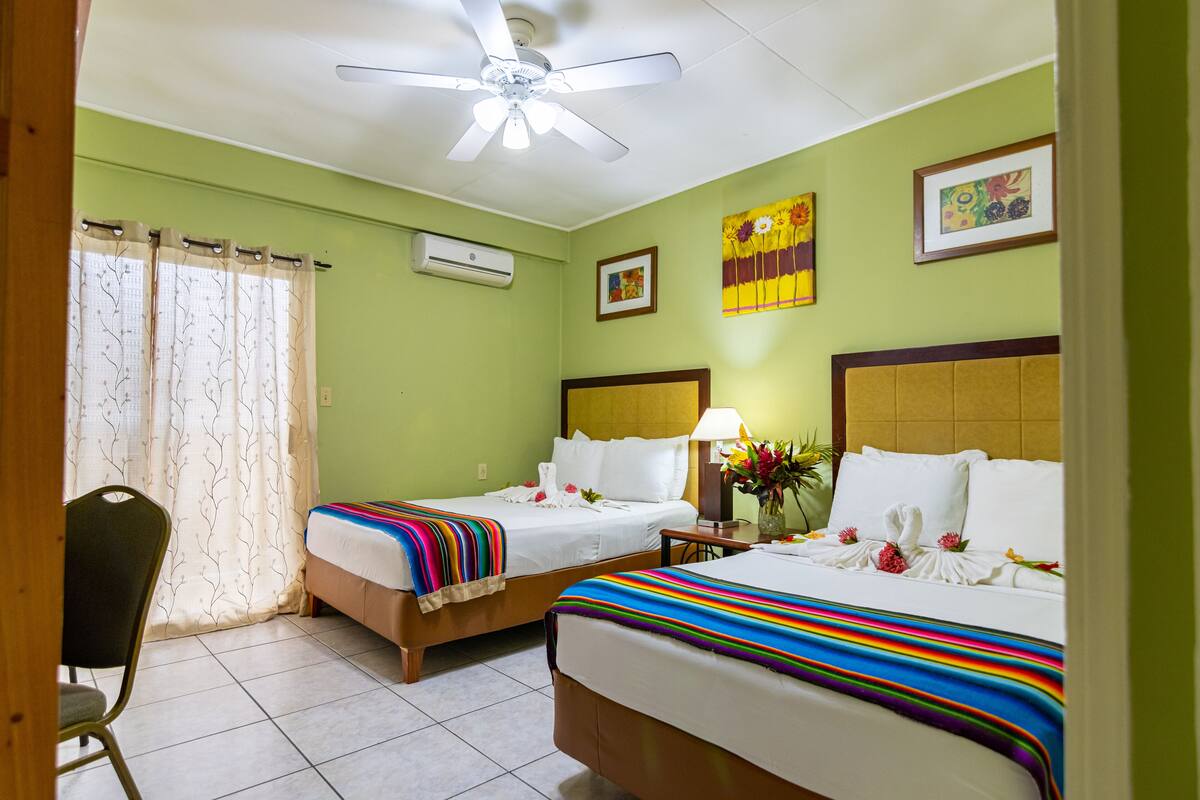 A hotel room with two beds, a ceiling fan, an air conditioning unit, and a chair.