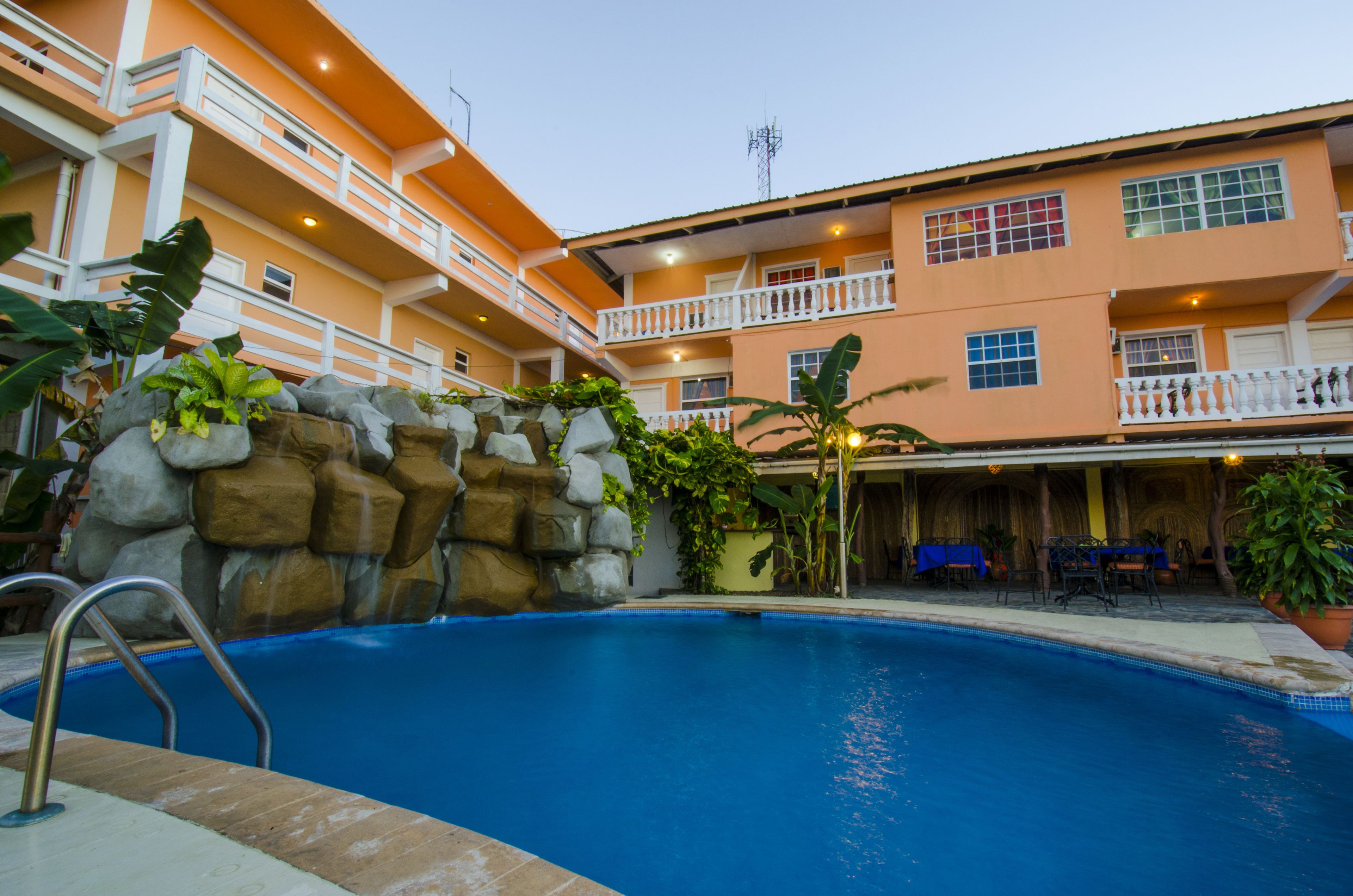 A hotel with a swimming pool, outdoor seating, and a multi-story building with balconies.