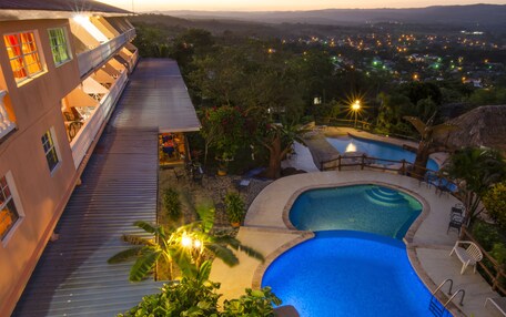 A hotel with a pool, outdoor seating, and a view of the city at dusk.