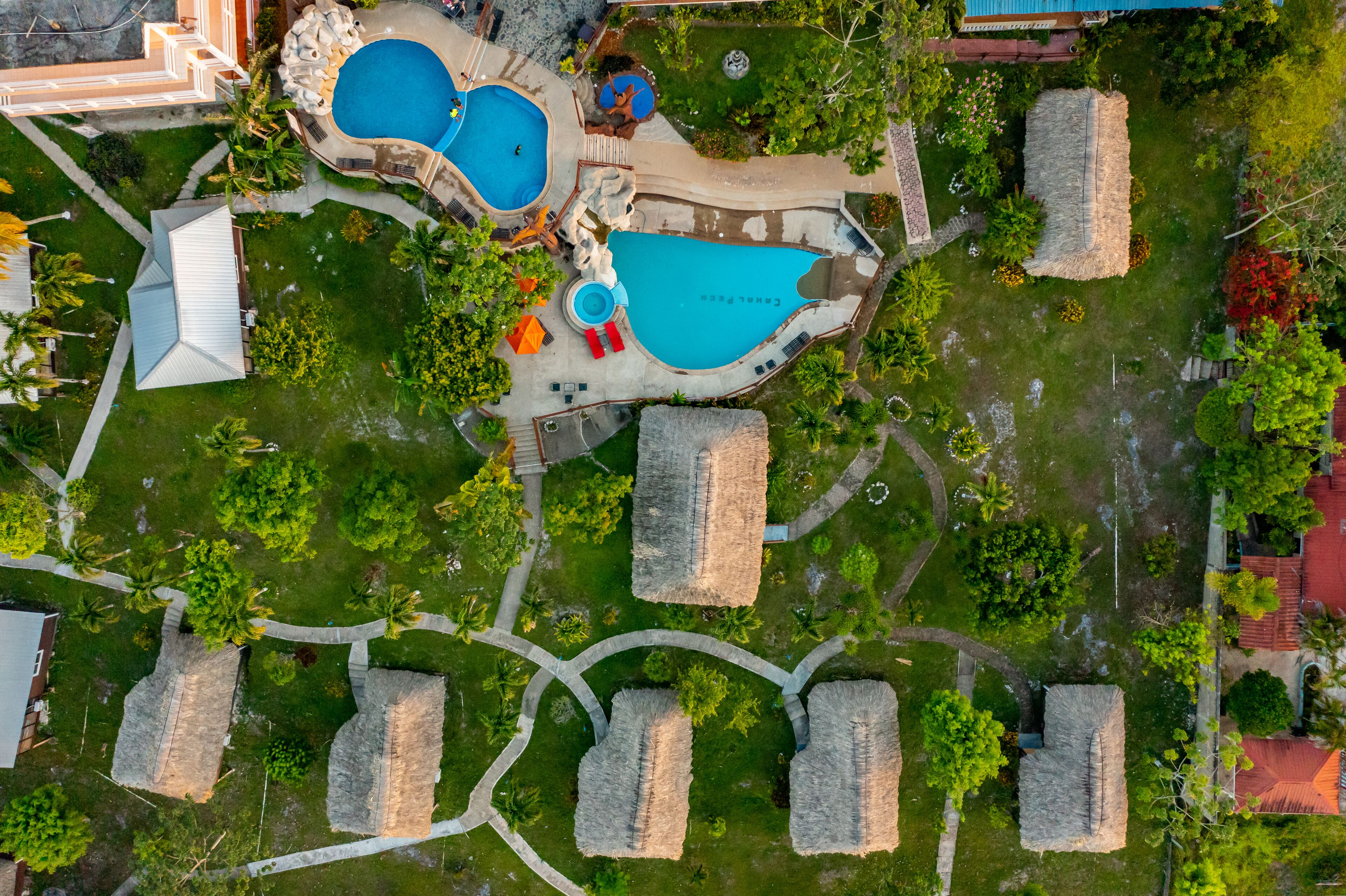 An aerial view of a resort with multiple swimming pools, thatched-roof huts, and well-maintained pathways.
