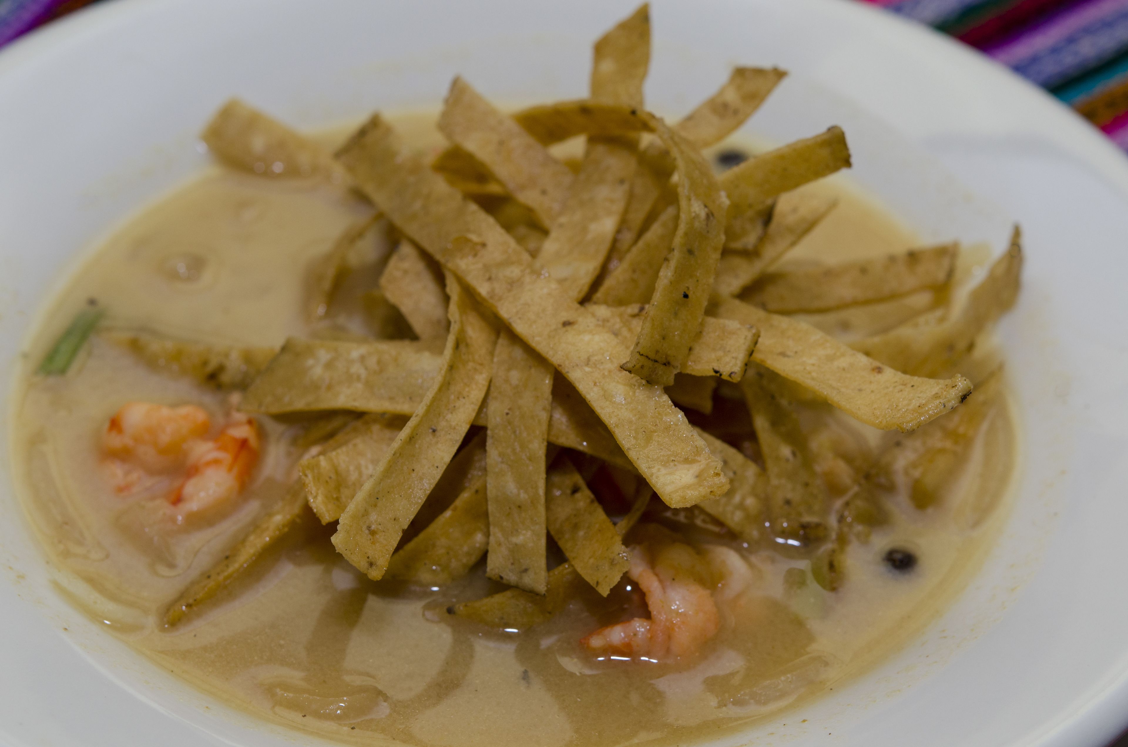 Un tazón de sopa con tiras de tortilla y camarones.