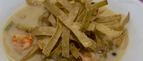 Un tazón de sopa con tiras de tortilla y camarones.