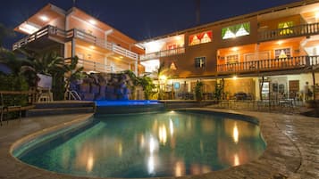 Um hotel com piscina, área de estar externa e um edifício com várias andares e sacadas.