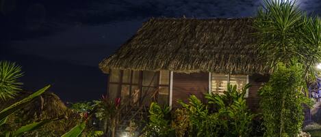 A thatched-roof house with a wooden exterior, surrounded by lush greenery and a small garden.
