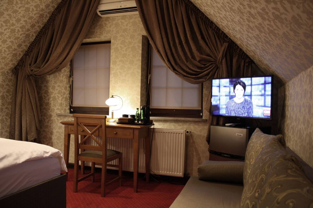 A hotel room with a bed, a desk with a chair, a television, and a radiator.
