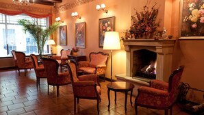 A warmly lit lounge area with patterned armchairs, a fireplace, and decorative wall art. - Hotel Petite Fleur - Adults only (Torun)