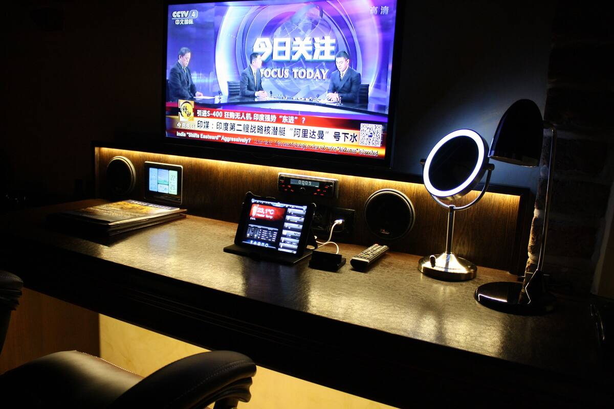 A hotel reception desk with a television displaying a news program, a digital clock, a mobile phone, and a ring light.