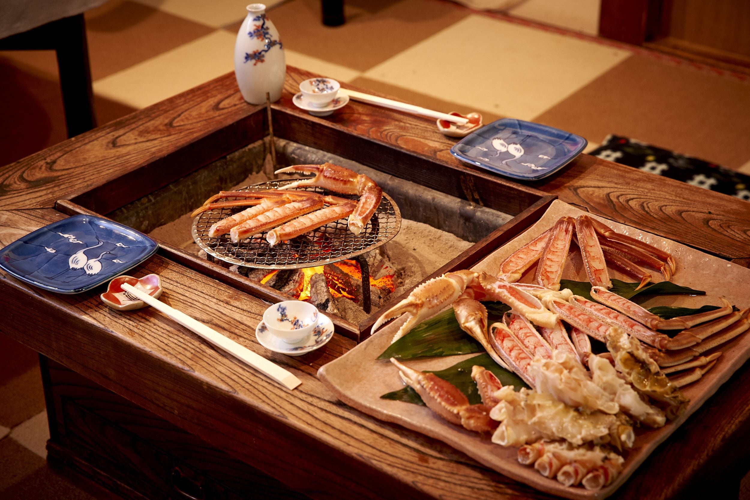 Uma mesa de madeira com mariscos dispostos em pratos e uma churrasqueira.
