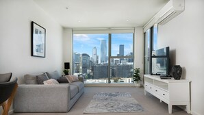 Una sala de estar moderna con un sofá gris, un mueble blanco para televisión y un ventanal con vistas a la ciudad.