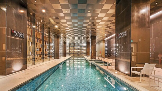 Una piscina interior con techo a cuadros, paredes de vidrio y un cartel que indica 'No Diving 12m Depth'.