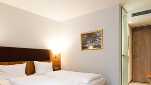 Una habitación de hotel con cama, mesita de noche, lámpara de pared, cuadro enmarcado y puerta.