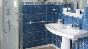 Un baño con ducha envuelta en vidrio, un lavabo blanco y paredes con azulejos azules.
