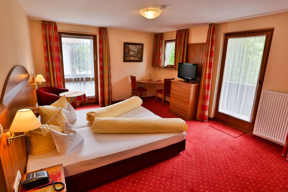 A hotel room with a bed, a desk, a chair, a television, and a window with curtains.