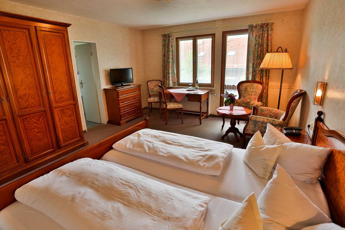A hotel room with two beds, a desk, a chair, a television, and a lamp.