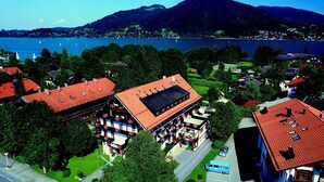A hotel with a red roof, multiple balconies with flower boxes, and a view of a lake and mountains in the background. - Hotel Askania (Bad Wiessee)