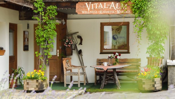 A cozy outdoor seating area with wooden furniture, potted plants, and a sign for 'VITAL-ALM Wellness & Massage'. - Hotel Askania (Bad Wiessee)