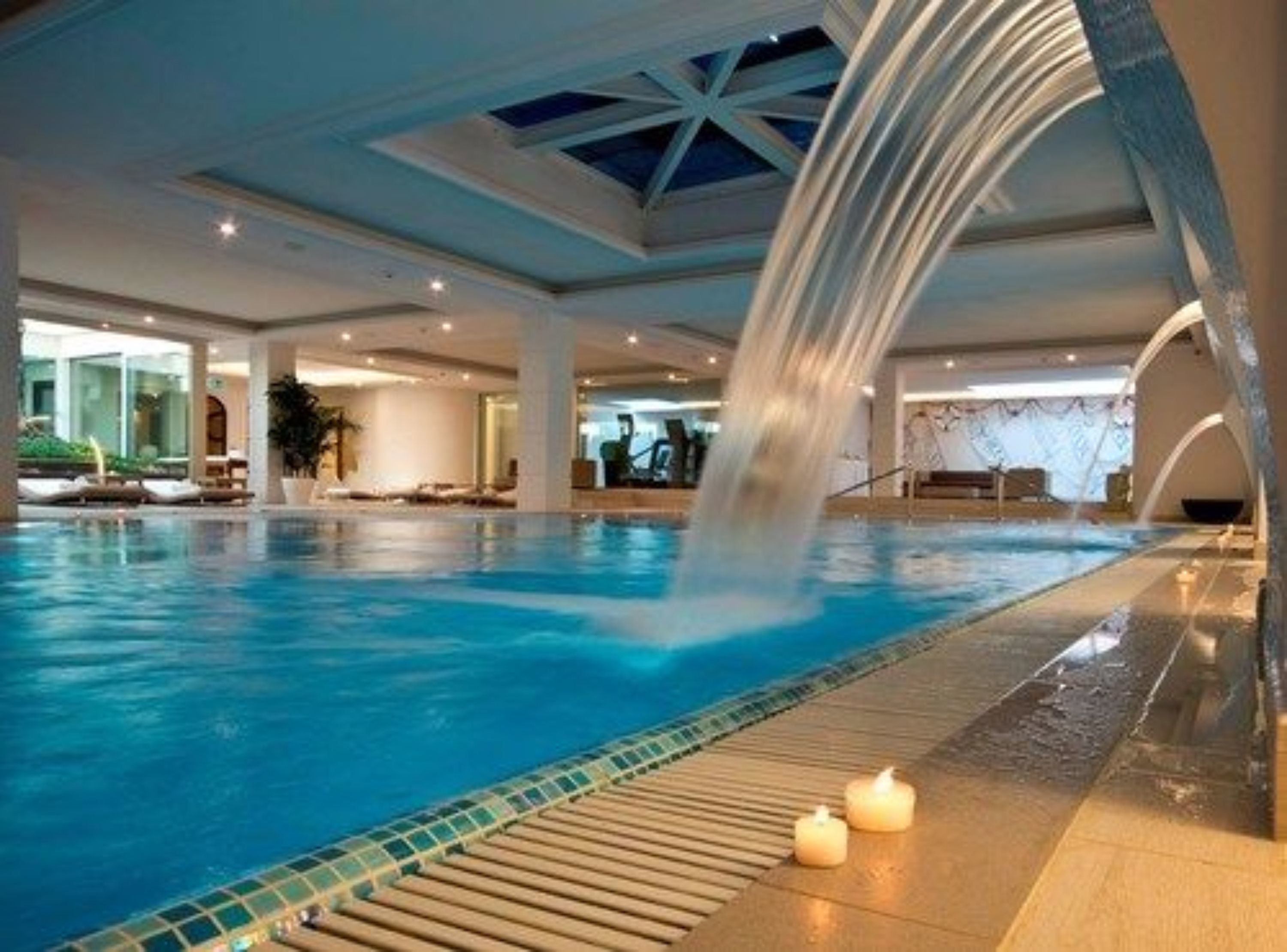 Une piscine intérieure agrémentée d’une cascade, de chaises longues et d’une terrasse carrelée.