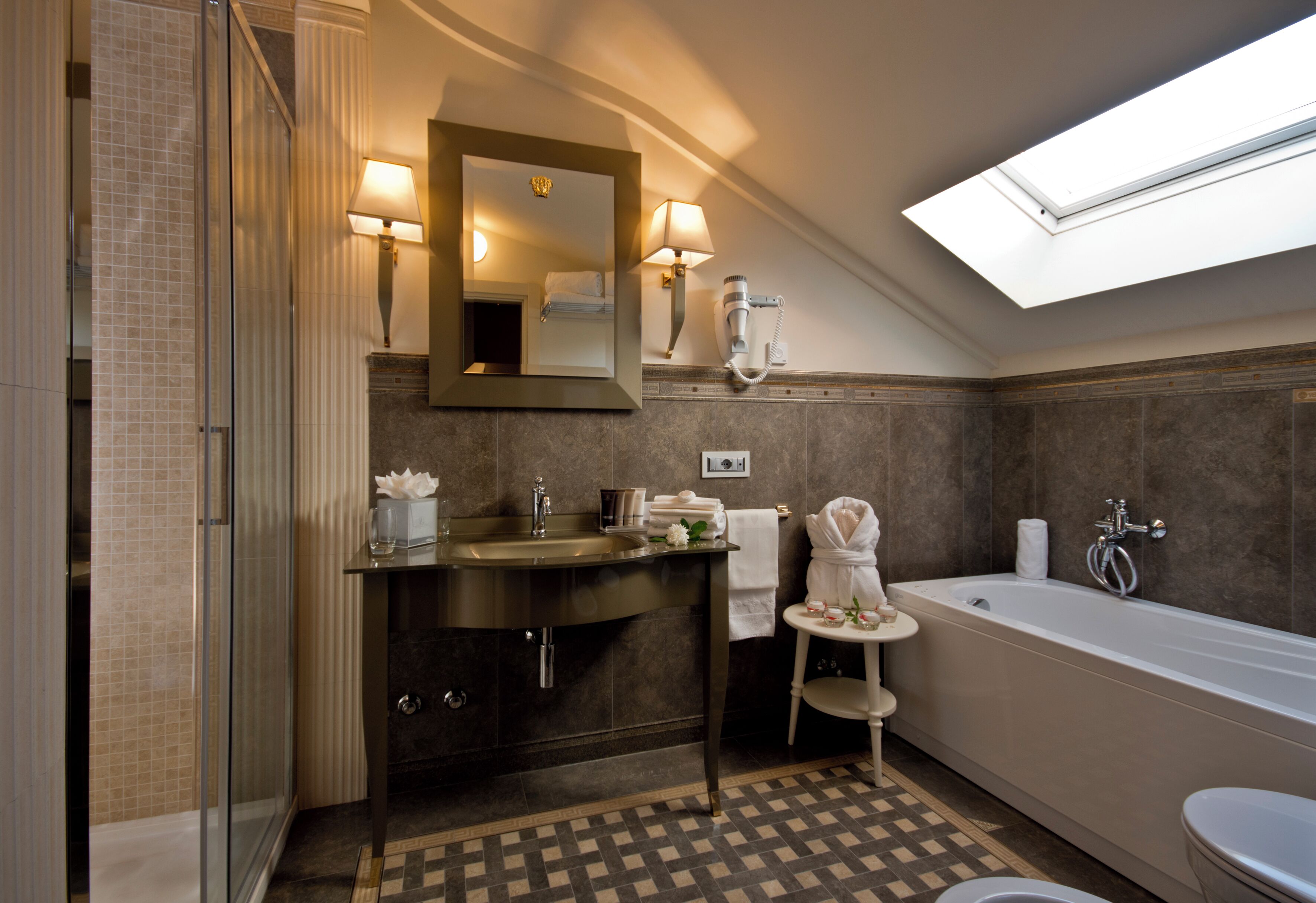 A modern bathroom with a glass shower enclosure, a freestanding bathtub, a vanity with a mirror, and a skylight above.