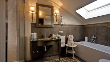 A modern bathroom with a glass shower enclosure, a freestanding bathtub, a vanity with a mirror, and a skylight above.