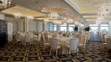 Une salle de banquet avec des tables rondes, des chaises blanches, des lustres et une moquette à motifs.