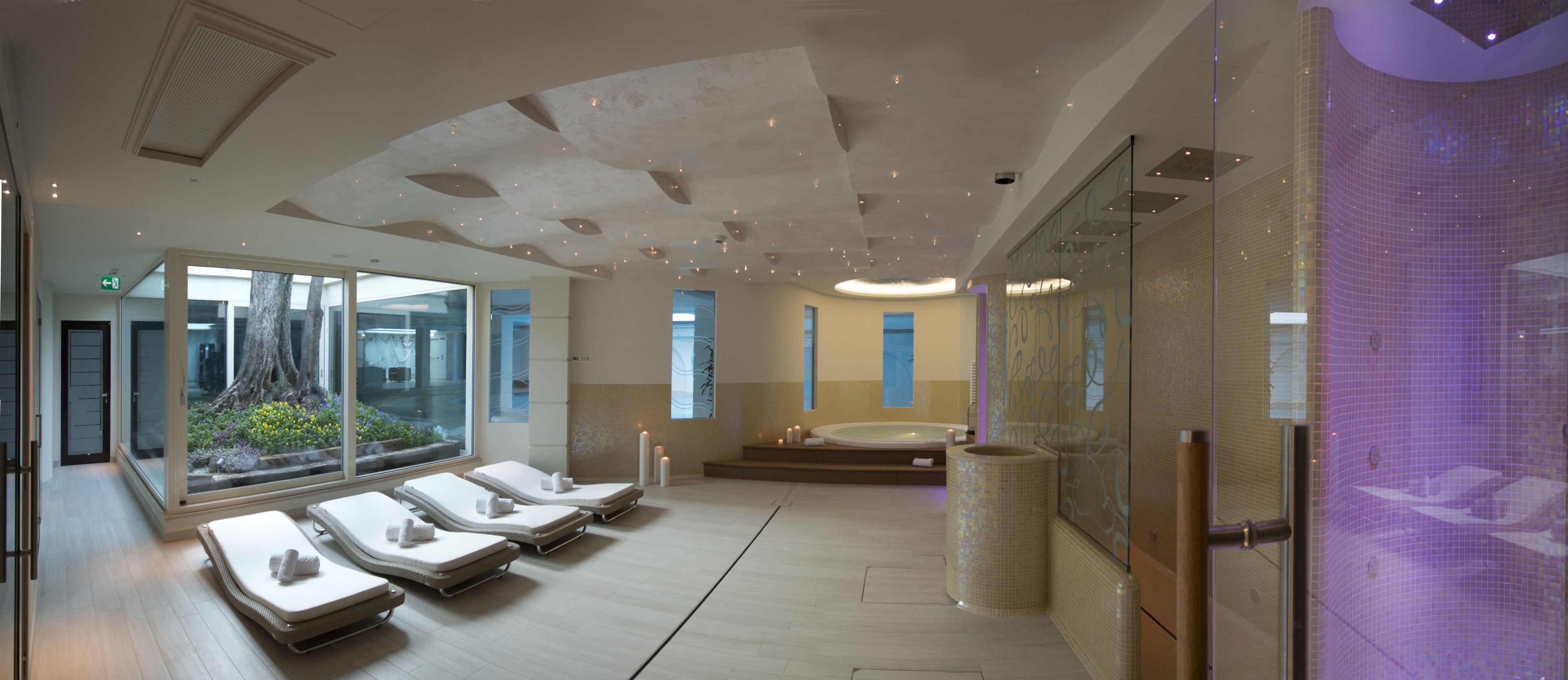 Ein modernes Spa mit Liegestühlen, einer großen Badewanne und einer Glaswand mit Blick auf Grünflächen.