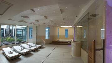 Ein modernes Spa mit Liegestühlen, einer großen Badewanne und einer Glaswand mit Blick auf Grünflächen.