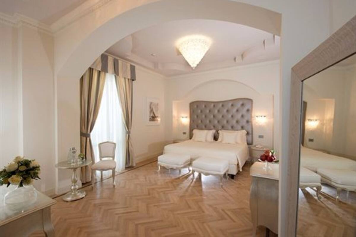 A hotel room with a large bed, a sitting area with a chair, a small table with a vase of flowers, and a large mirror.