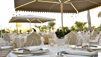 Mesa lista para comer al aire libre con una sombrilla, rodeada de sillas y mesas.
