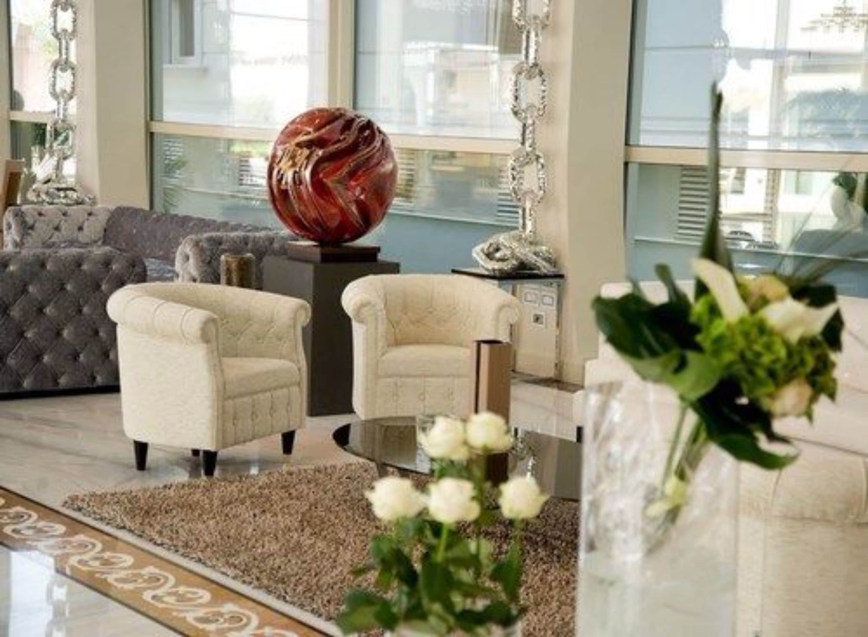 Una sala de estar moderna con un sofá capitonado gris, dos sillones color crema, una mesa de centro de vidrio y una escultura decorativa de cristal.