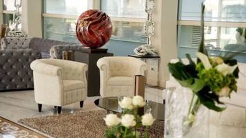 Una sala de estar moderna con un sofá capitonado gris, dos sillones color crema, una mesa de centro de vidrio y una escultura decorativa de cristal.