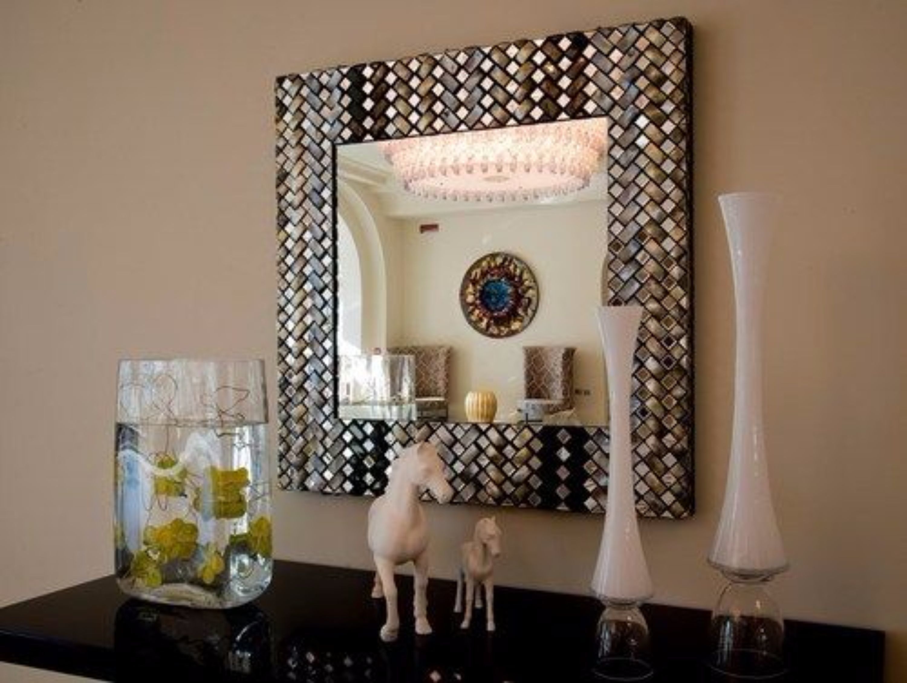 A mirror with a geometric pattern, a vase with yellow flowers, and a small horse figurine on a black surface.