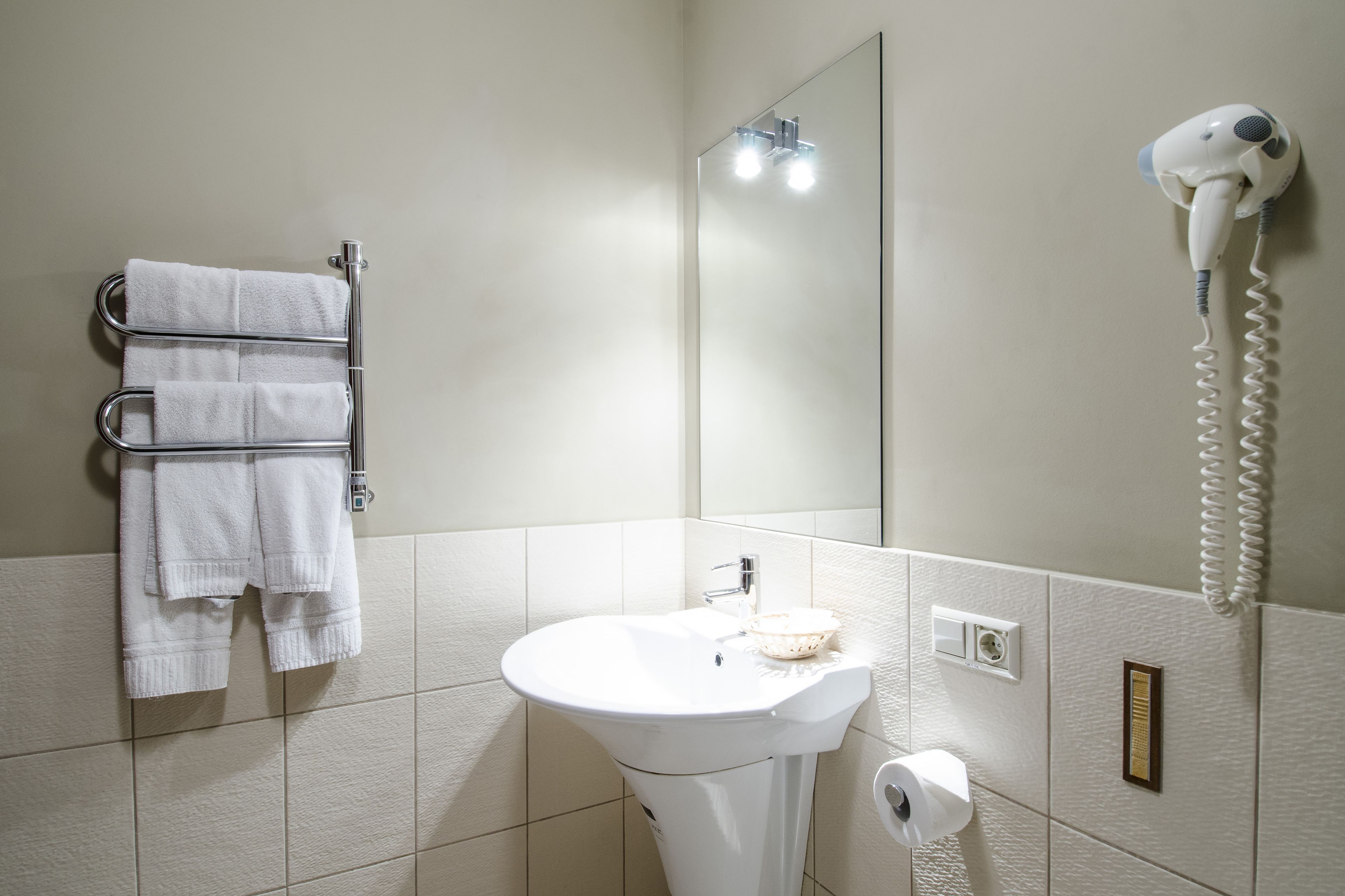 A bathroom with a sink, towel rack, mirror, hairdryer, and a light switch.