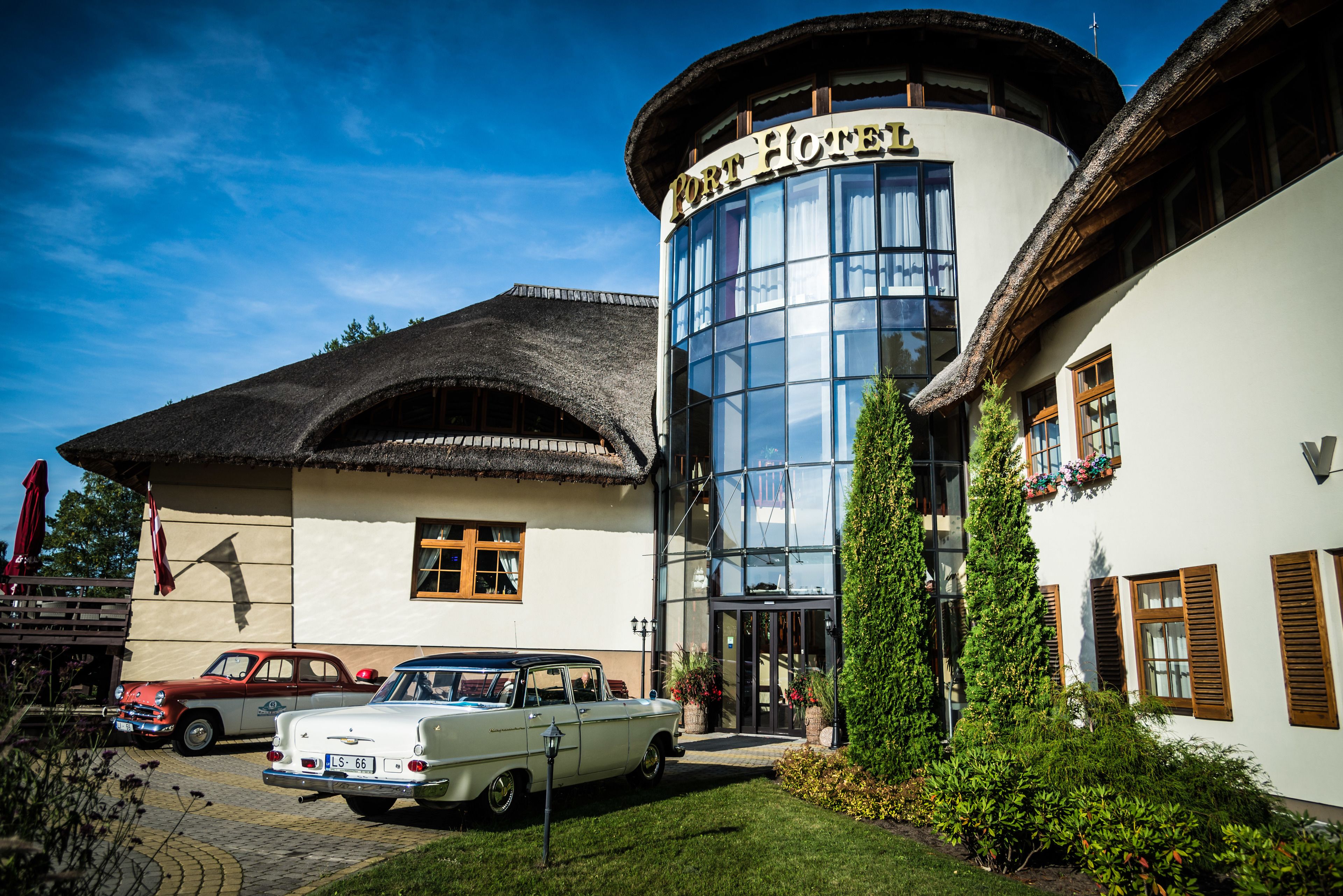 A hotel with a traditional facade, a glass entrance, and classic cars parked in front.