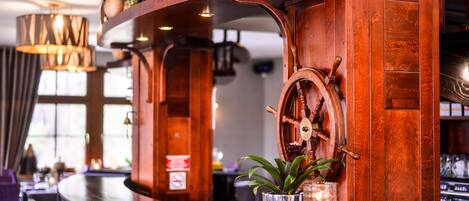 Uma área de bar com balcão de madeira, uma roda giratória e um vaso de planta.