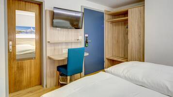Una habitación de hotel con cama, escritorio, silla, televisor y armario.