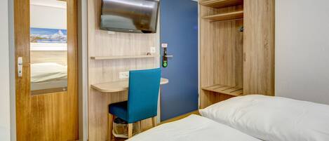 A hotel room with a bed, a desk, a chair, a TV, and a wardrobe.