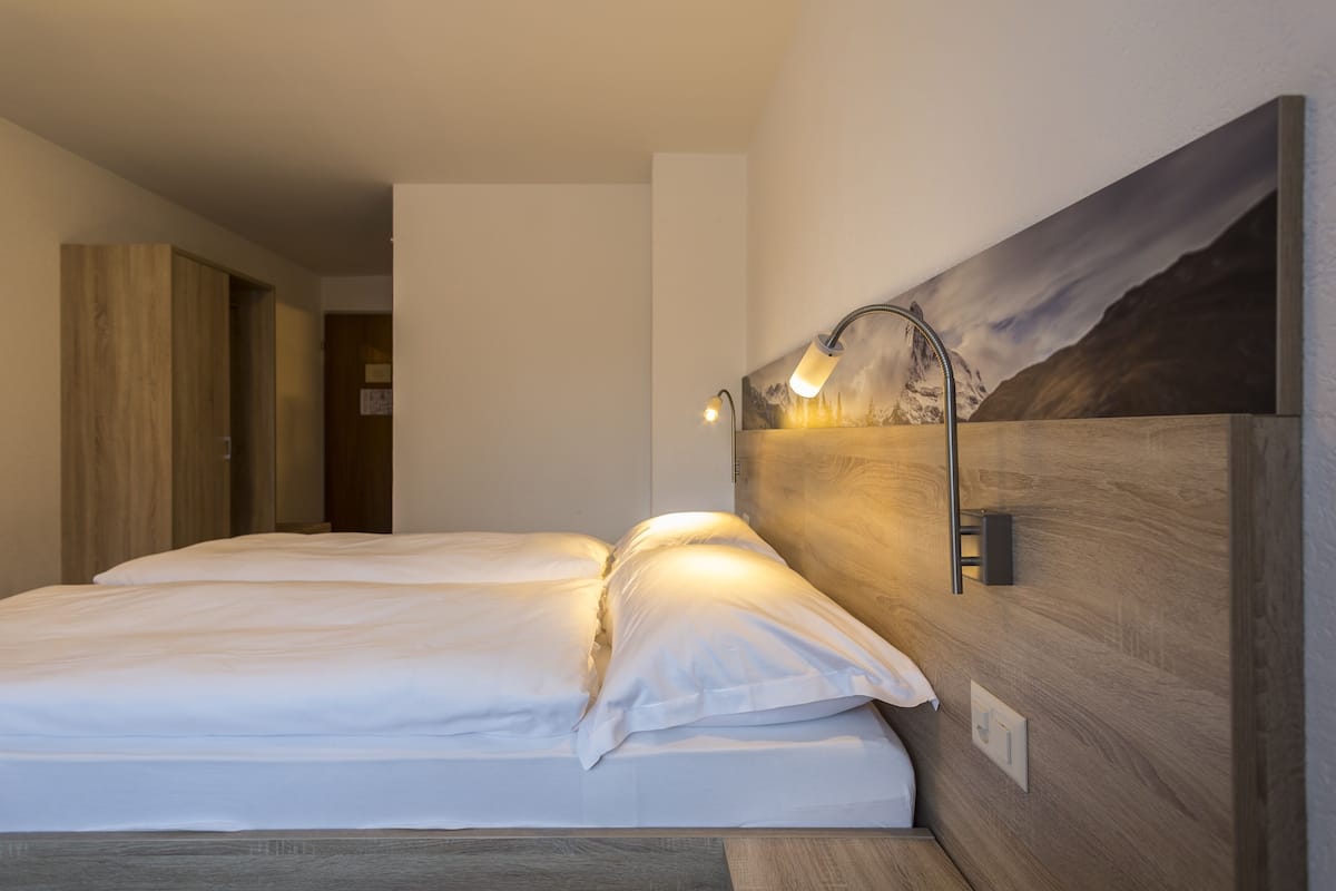Habitación de hotel moderna con cabecera de madera, un cuadro de un paisaje montañoso y una lámpara de noche.