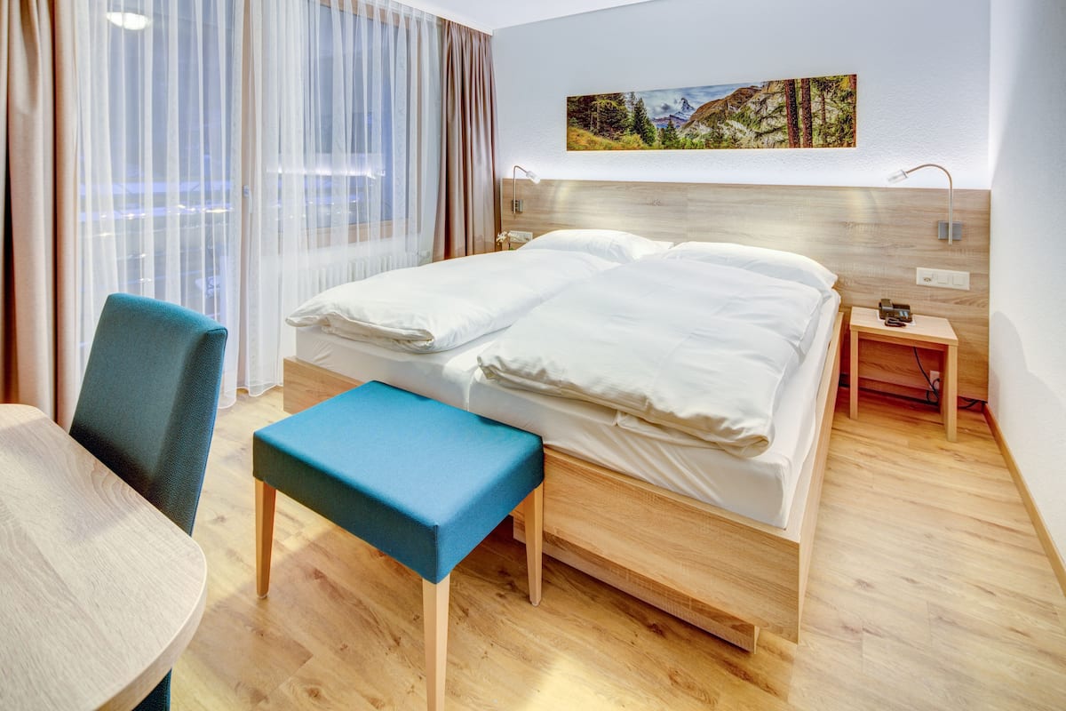 Habitación de hotel con cama de madera, un escritorio, una silla y un banco.