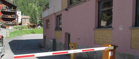 Un bâtiment à la façade rose, doté d’une entrée fermée par un portail et surmonté d’une église visible au loin.