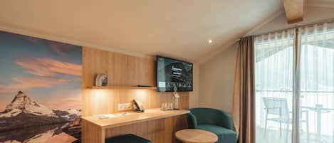 A modern room with a wooden desk, a blue chair, a small stool, and a large wall mural of a mountain landscape.